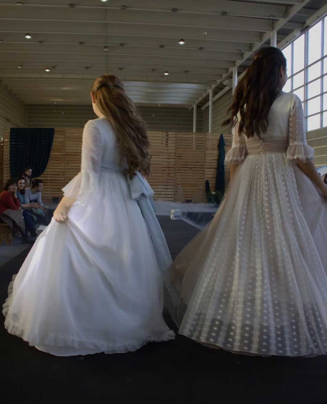 Dos niñas de espaldas vestidas de traje de comunión y peinada con pelo semi suelto.